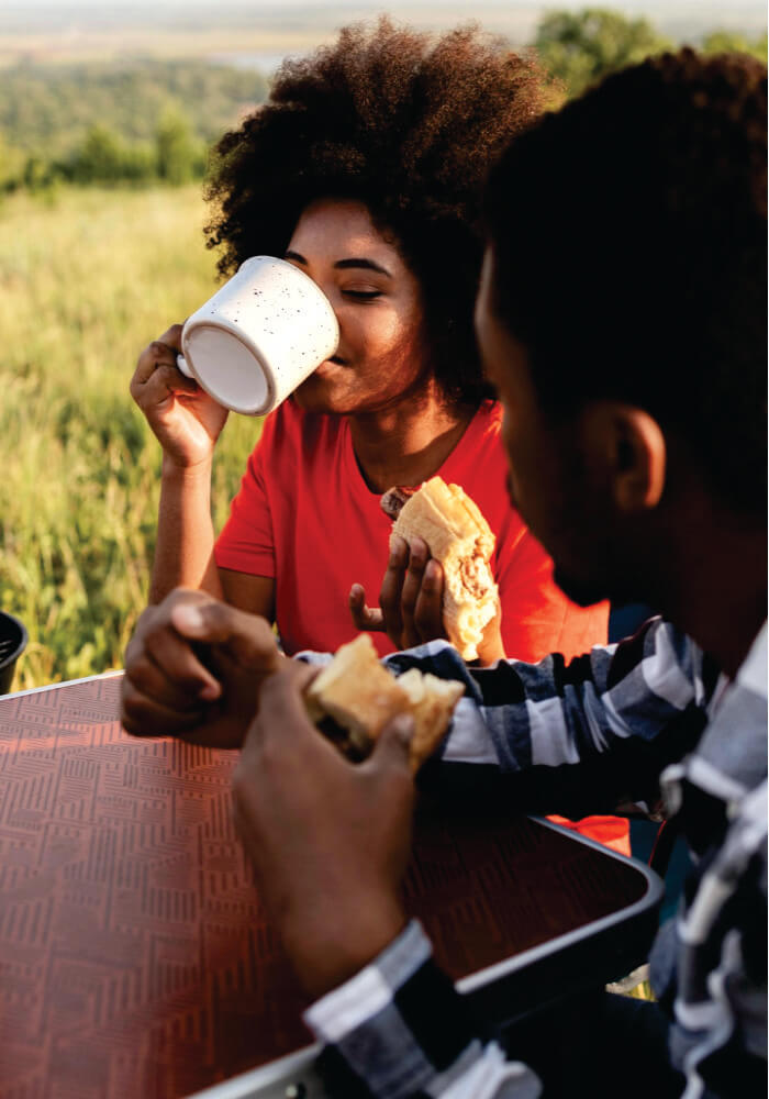 Two people enjoying food and drinks outdoors in a natural setting on full-day safari game drives in Masai Mara