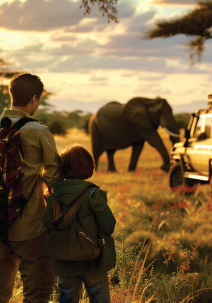 Father and son watching an elephant walking near a beige Jeep in Masai Mara on 2 nights affordable family accommodation in Masai Mara