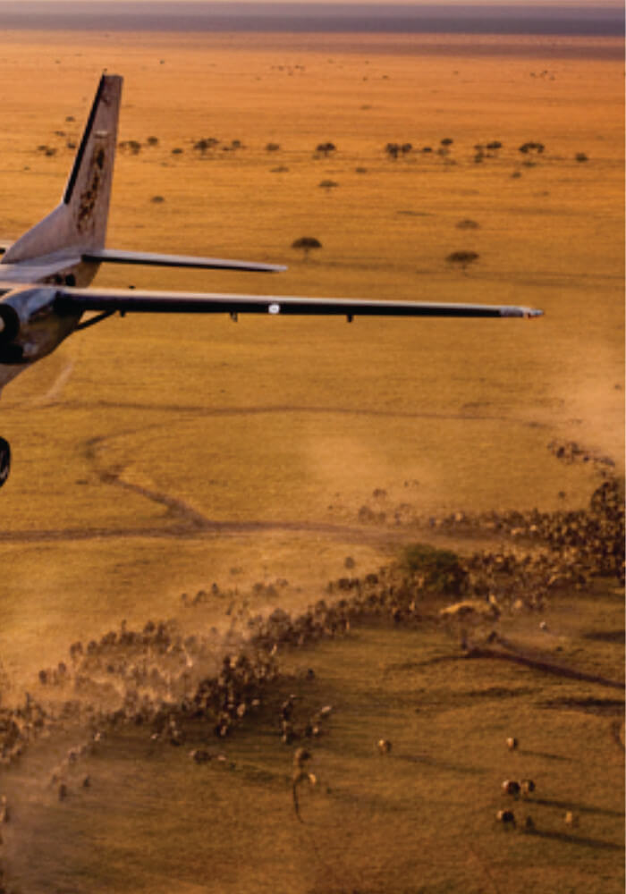 Aerial view of a large airplane flying over a landscape with trees and open fields.