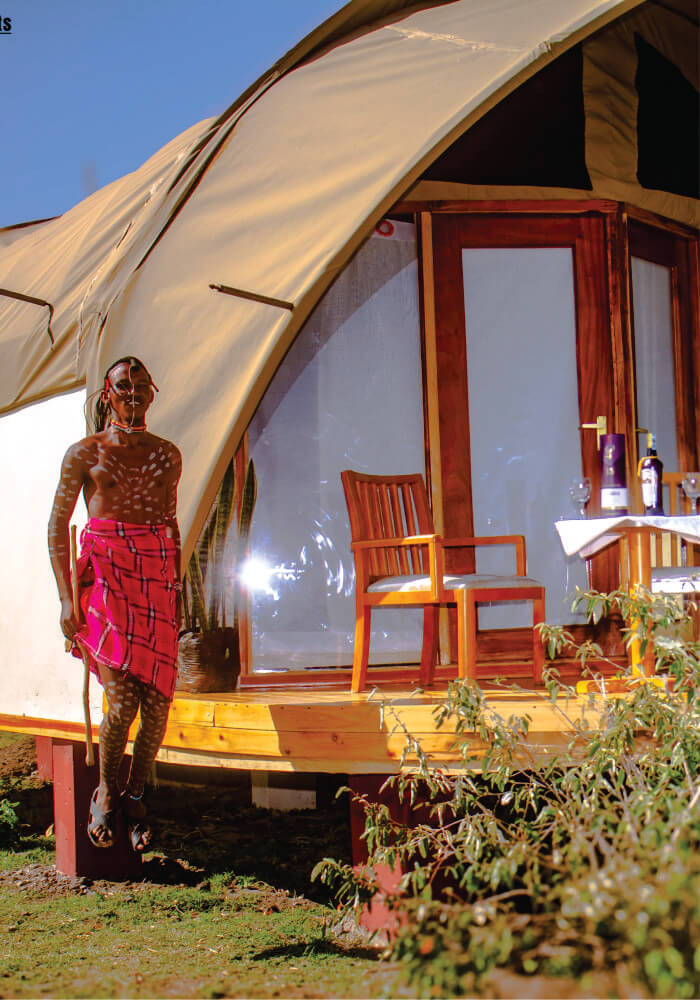 Young man in red Maasai Shuka jumping near wine table setting on wooden verandah near on 2 nights Masai Mara budget accommodation