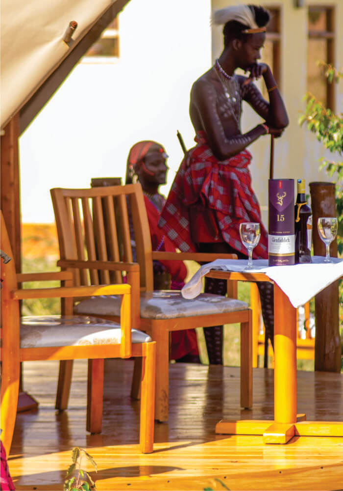 Two people standing near a wine table setting on a wooden verandah on budget Lodge accommodation in Masai Mara hotels for groups