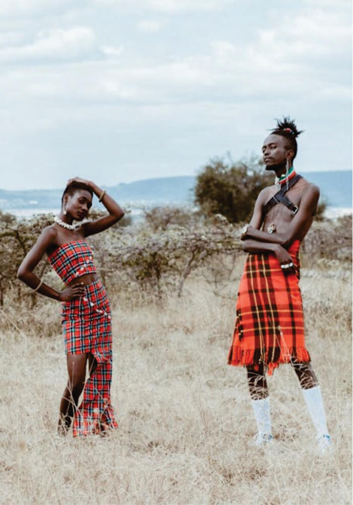 Two people in traditional African attire standing in a natural landscape.