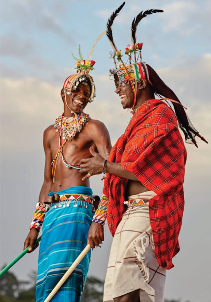 Two individuals in traditional African attire with colorful headdresses against a cloudy sky.
