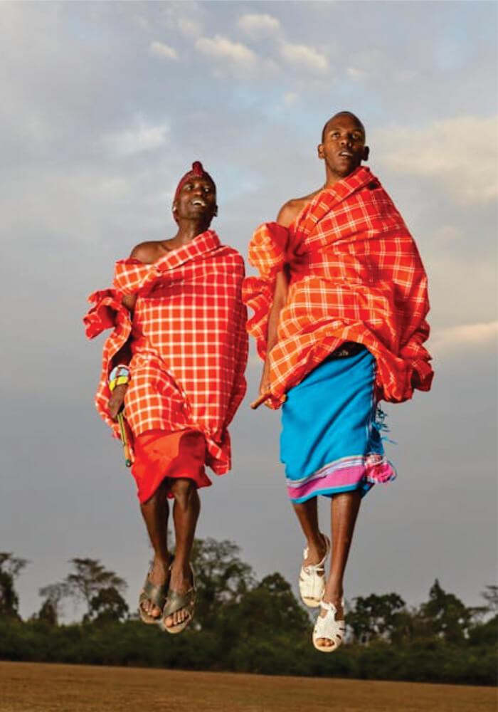 Two individuals in traditional Masai clothing jumping against a sky background