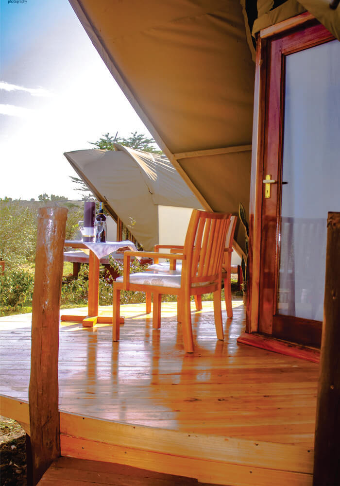 Clear view of wine table setting on wooden verandah near in tented camp with beige canvas on 3 nights accommodation in Masai Mara